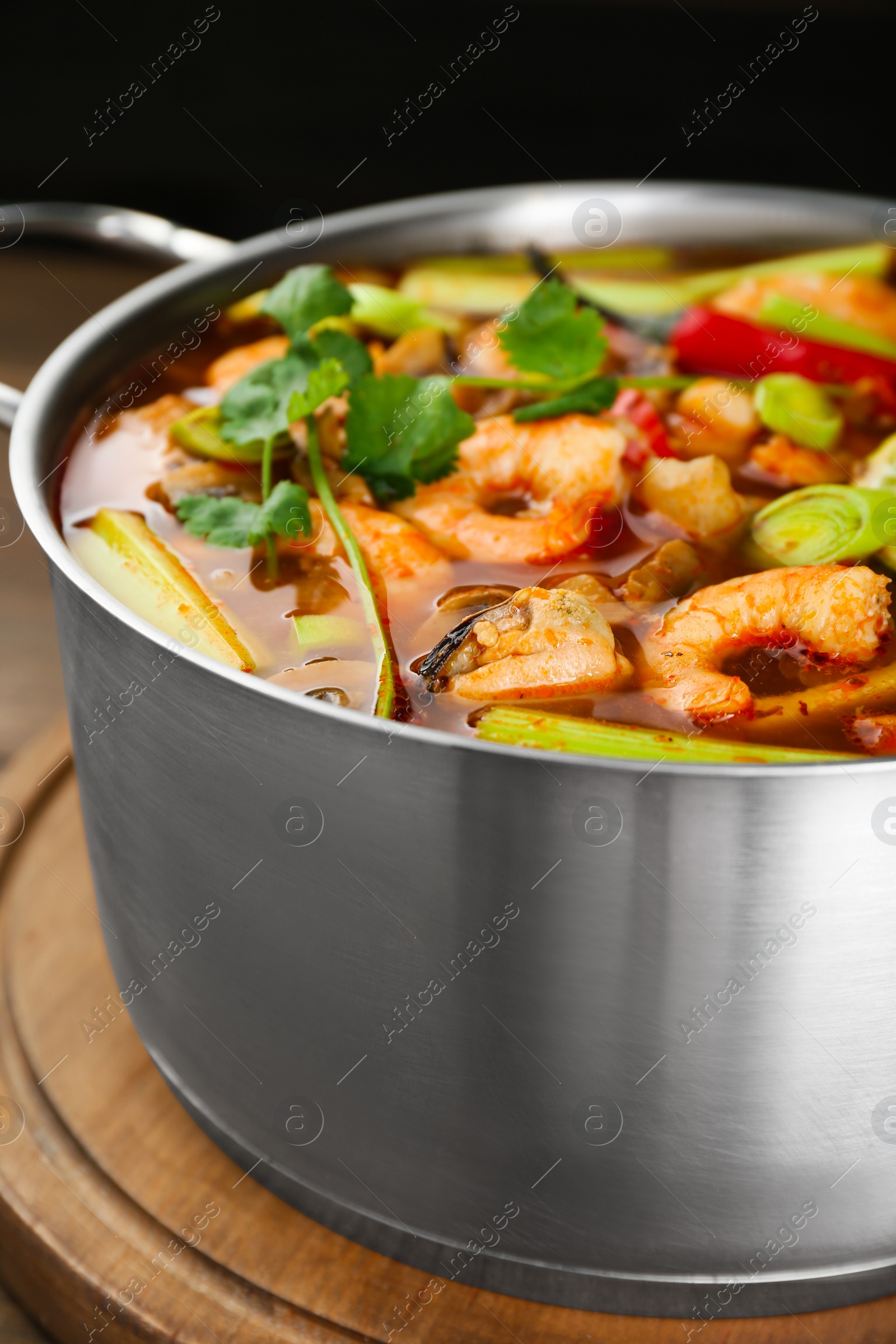 Photo of Saucepan with delicious Tom Yum soup on wooden board, closeup