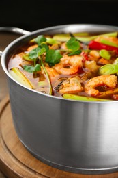 Saucepan with delicious Tom Yum soup on wooden board, closeup