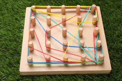 Wooden geoboard with rubber bands on artificial grass, closeup. Educational toy for motor skills development