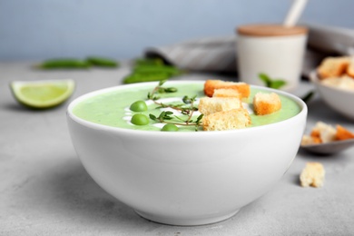 Photo of Green pea soup with croutons in bowl on table