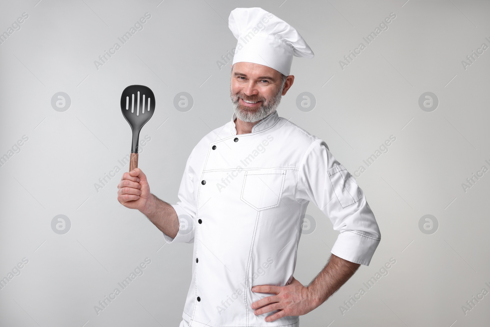 Photo of Happy chef in uniform with spatula on grey background