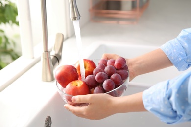 Photo of Woman washing fresh grapes and nectarines in kitchen sink, closeup