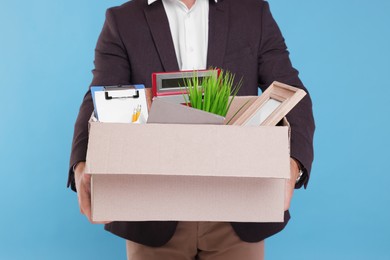 Unemployed man with box of personal office belongings on light blue background, closeup