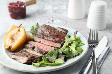 Photo of Delicious roasted beef meat served with caramelized pear and greens on light table, closeup