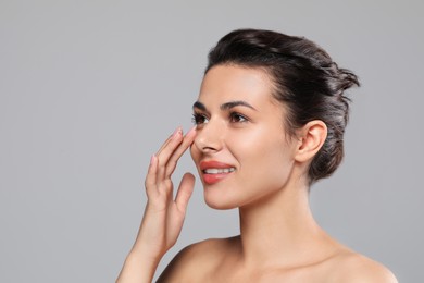 Photo of Woman applying cream under eyes on grey background, space for text. Skin care