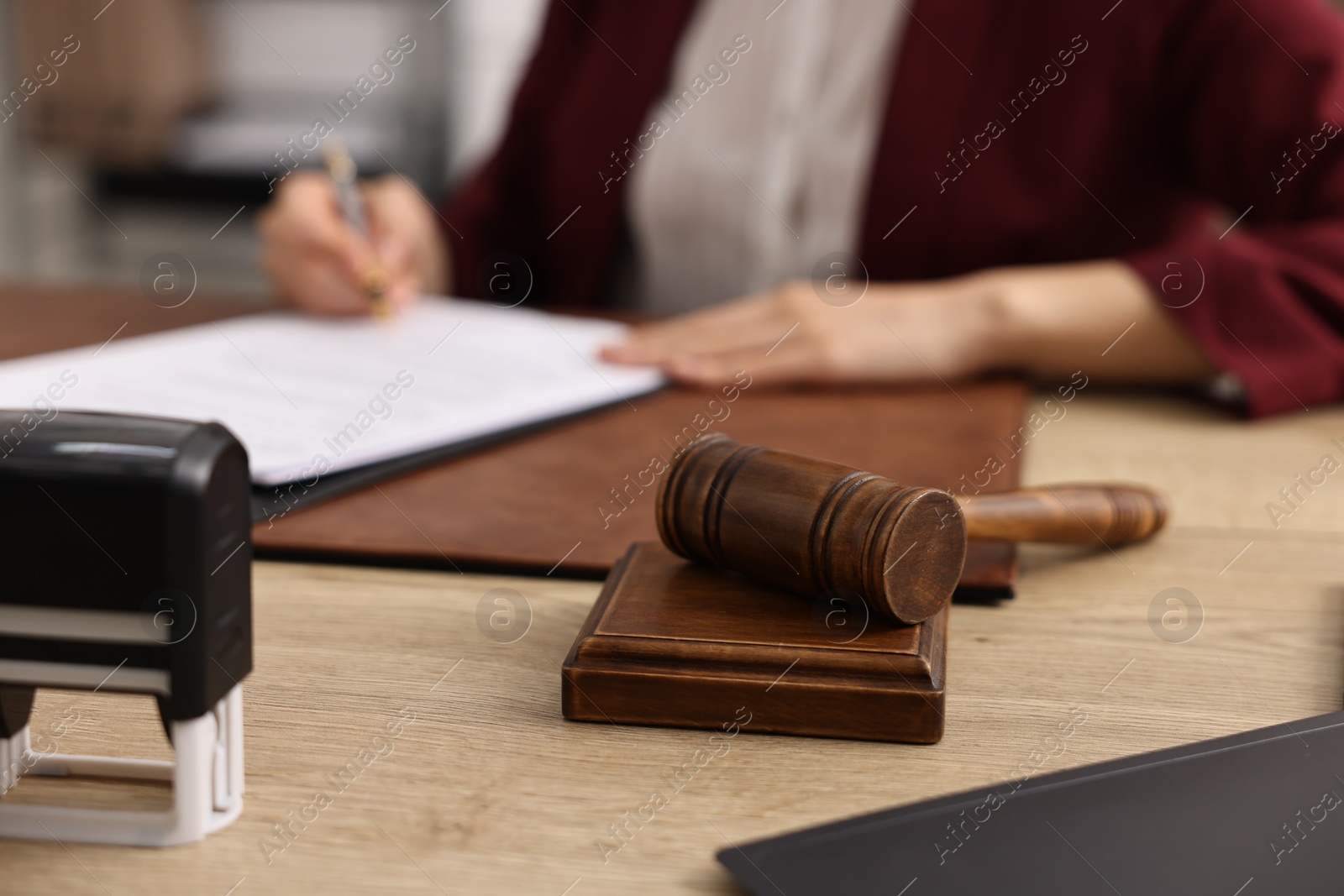 Photo of Notary signing document at wooden table in office, focus on gavel