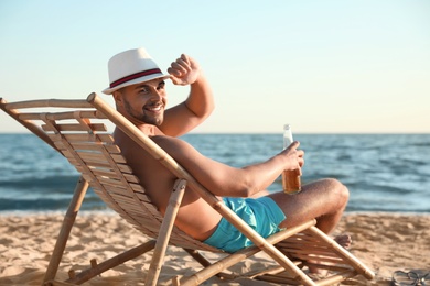 Young man relaxing in deck chair on beach near sea
