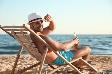 Photo of Young man relaxing in deck chair on beach near sea