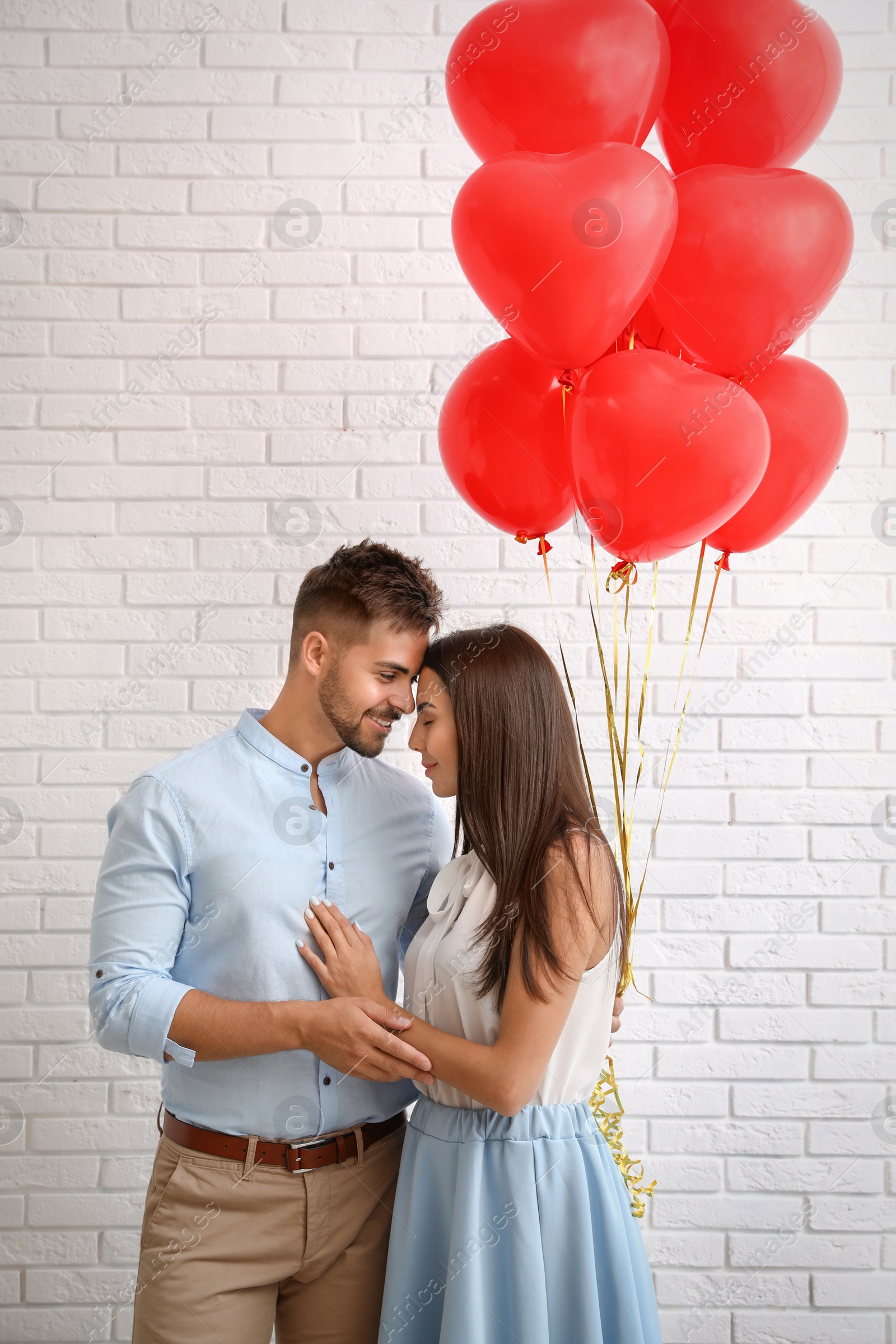 Photo of Young couple with air balloons near white brick wall. Celebration of Saint Valentine's Day