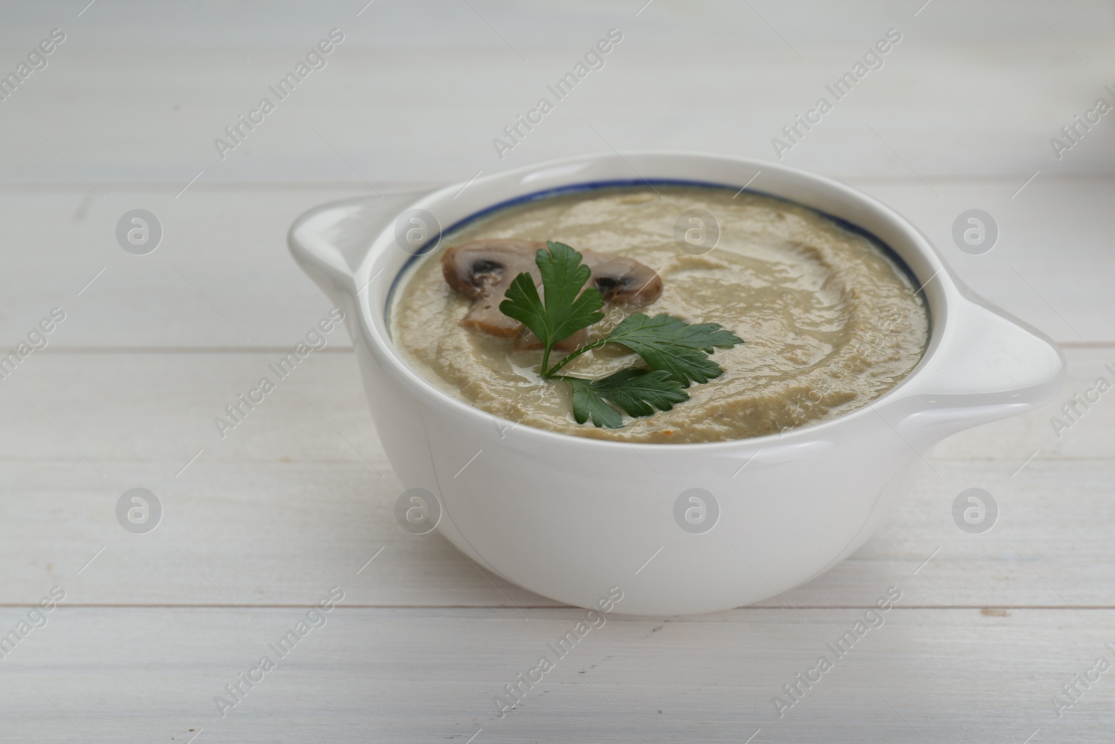 Photo of Delicious mushroom cream soup with parsley on white wooden table