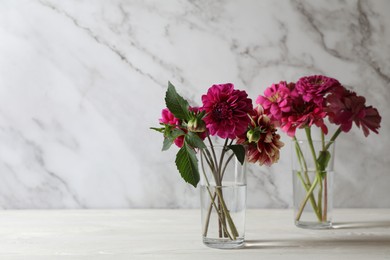 Bouquet of beautiful wild flowers and leaves in vases on white wooden table against marble background. Space for text