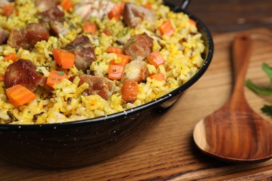 Delicious pilaf with meat and carrot served on wooden table, closeup