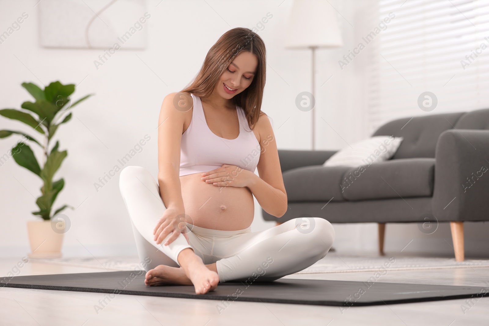 Photo of Pregnant woman sitting on yoga mat at home