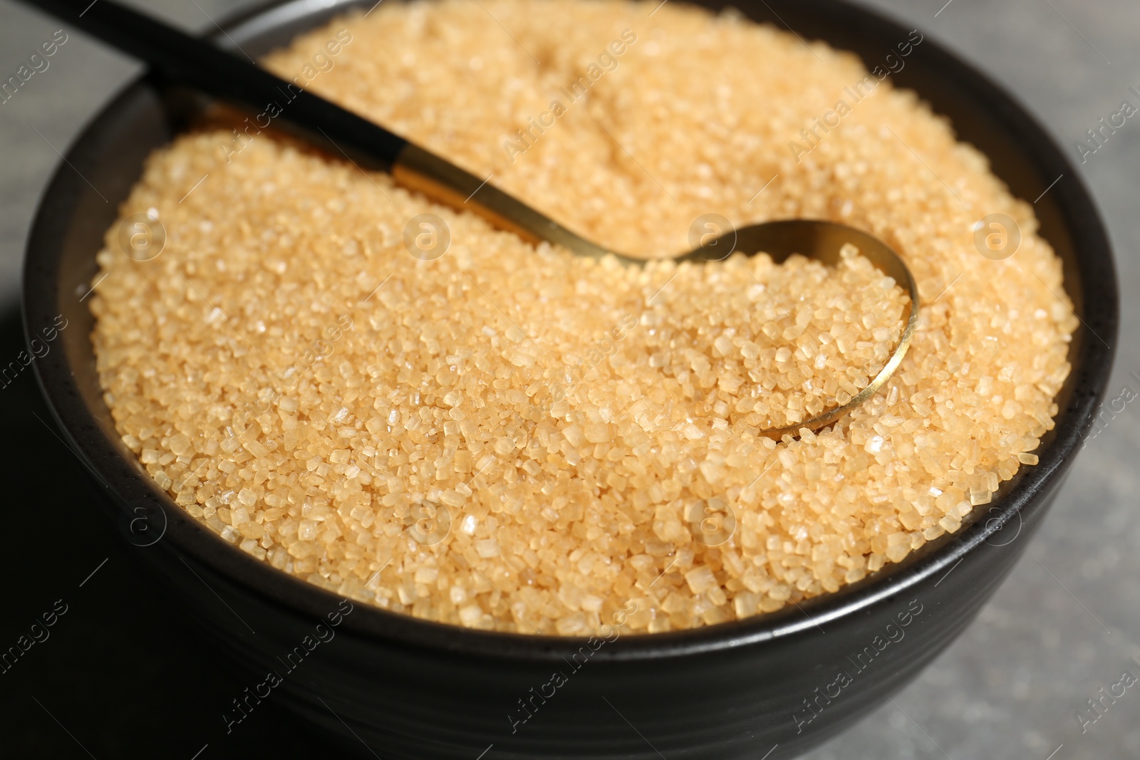 Photo of Brown sugar in bowl and spoon on grey table, closeup