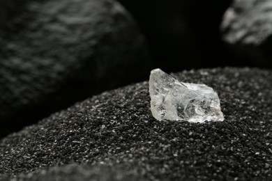 Photo of Shiny rough diamond on decorative black sand, closeup. Space for text