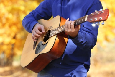 Photo of Young man playing guitar in autumn park, closeup