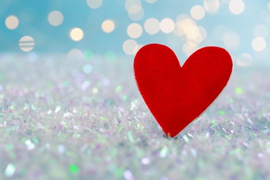 Red decorative heart on glitter against blurred lights, closeup. Space for text