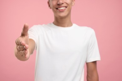 Photo of Happy man welcoming and offering handshake on pink background, selective focus