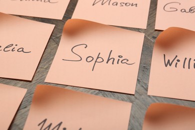 Photo of Paper stickers with different names on wooden table, closeup. Choosing baby's name