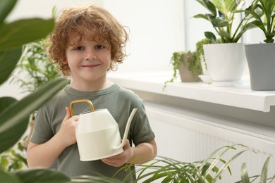 Photo of Cute little boy holding watering can near beautiful green plants at home. House decor