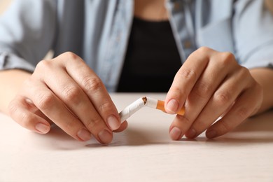 Photo of Stop smoking. Woman holding broken cigarette at table, closeup