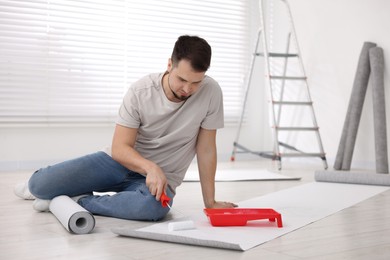 Man applying glue onto wallpaper sheet in room