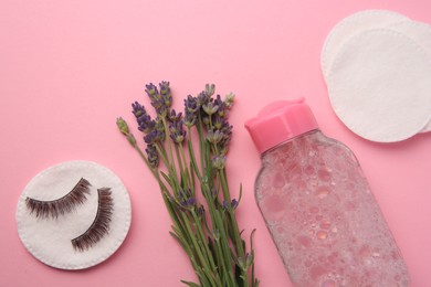 Photo of Bottle of makeup remover, lavender, cotton pads and false eyelashes on pink background, flat lay