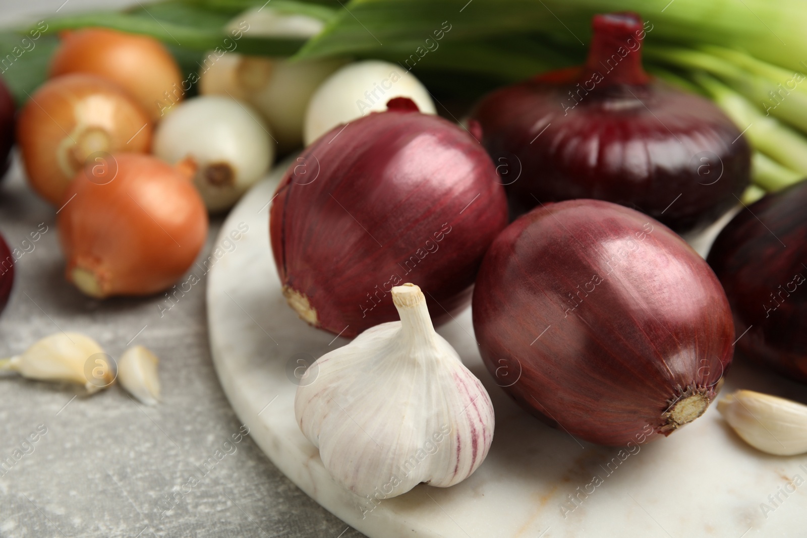 Photo of Fresh onion bulbs, leek and garlic on grey table, closeup