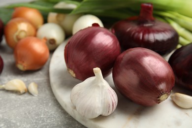 Photo of Fresh onion bulbs, leek and garlic on grey table, closeup