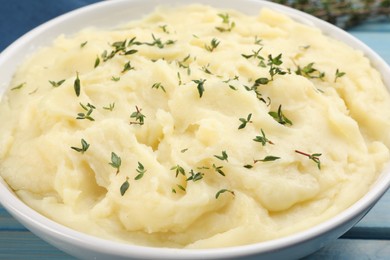 Photo of Bowl of tasty mashed potato with rosemary on light blue wooden table, closeup