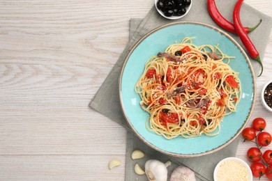 Photo of Plate of delicious pasta with anchovies, tomatoes and parmesan cheese near ingredients on white wooden table, flat lay. Space for text