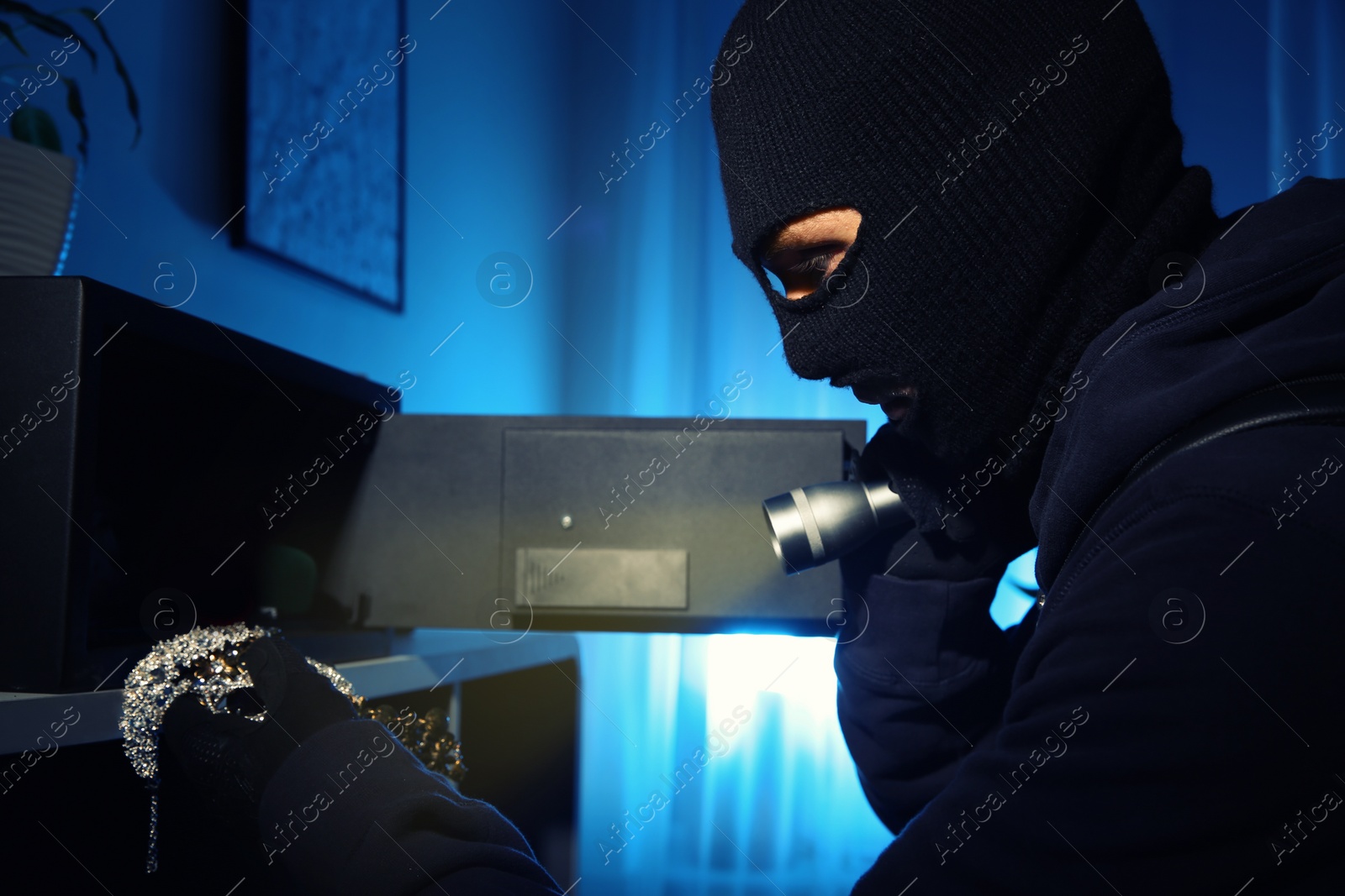 Photo of Thief taking jewelry out of steel safe indoors at night