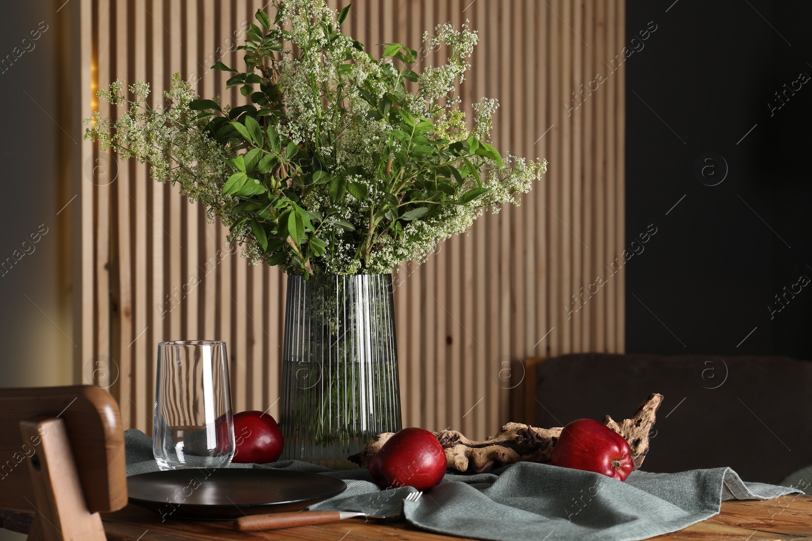 Photo of Set of clean dishware, ripe red apples and flowers on wooden table in stylish dining room