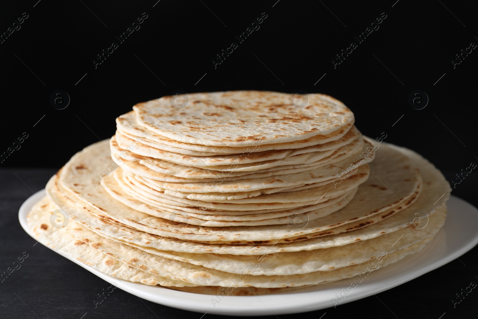 Photo of Many tasty homemade tortillas on black wooden table, closeup