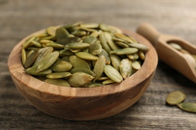 Photo of Bowl and scoop with peeled pumpkin seeds on wooden table, closeup
