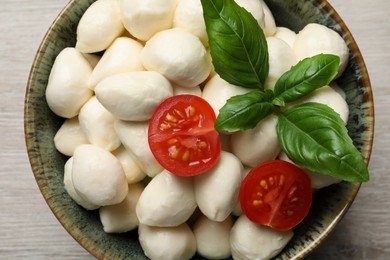 Delicious mozzarella balls, tomatoes and basil leaves in bowl on white wooden table, top view