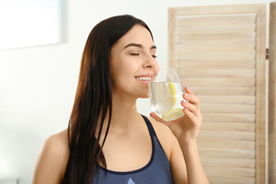 Beautiful sportive woman drinking fresh lemon water indoors