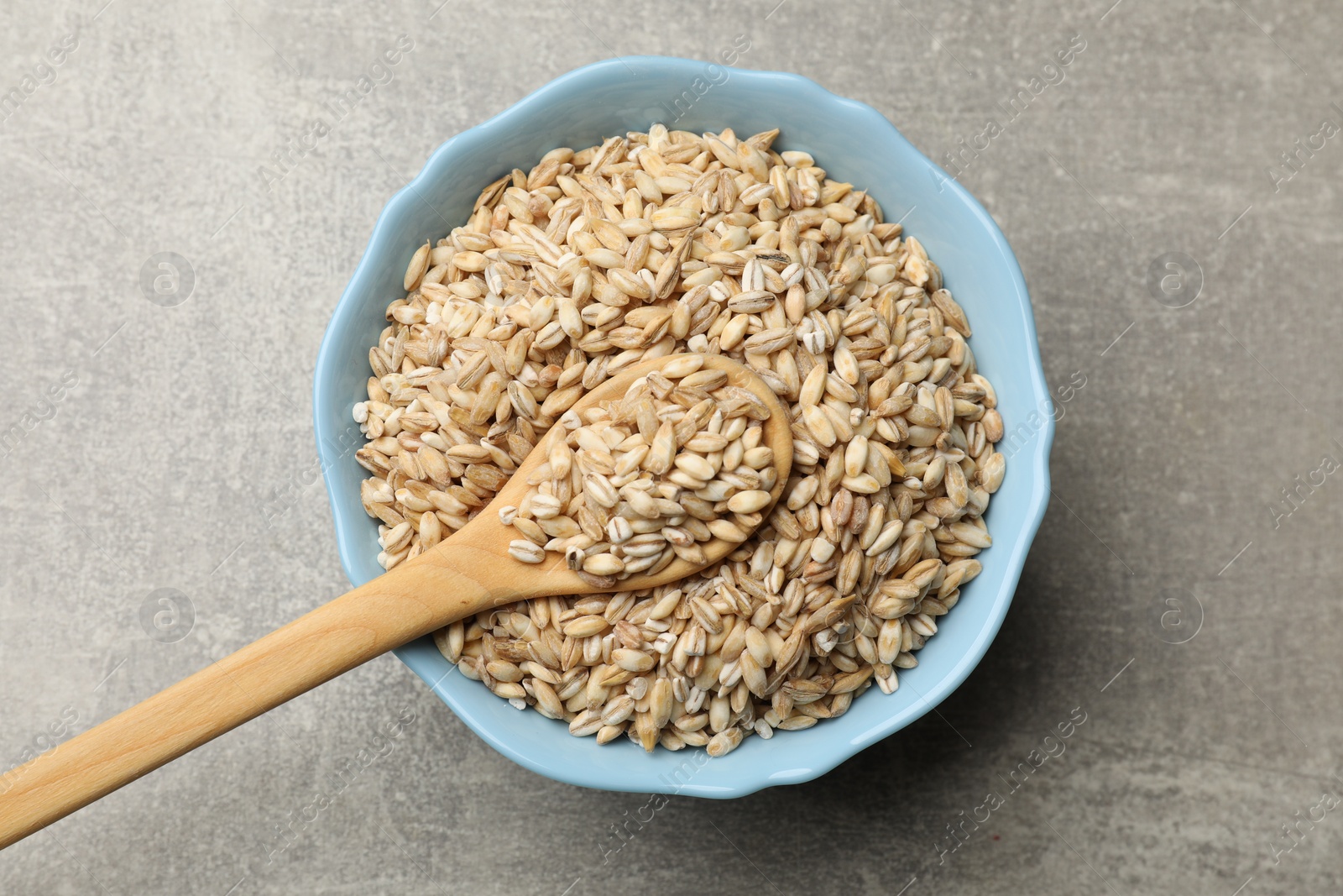 Photo of Dry pearl barley in bowl and spoon on gray table, top view