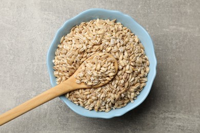 Photo of Dry pearl barley in bowl and spoon on gray table, top view