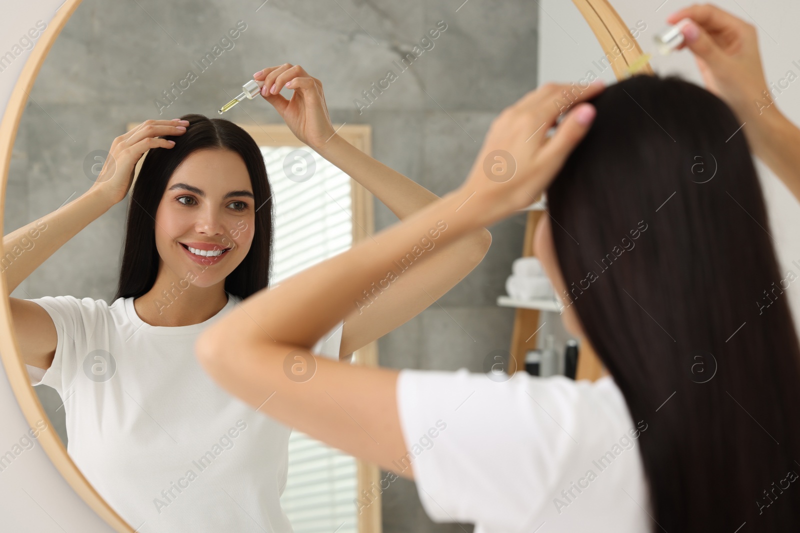 Photo of Beautiful woman applying hair serum in bathroom. Cosmetic product