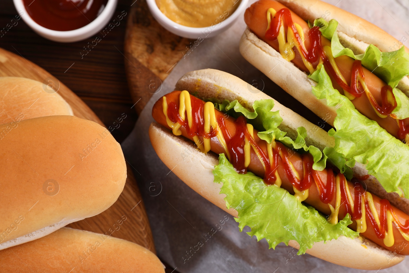 Photo of Tasty hot dogs and ingredients on wooden table, flat lay