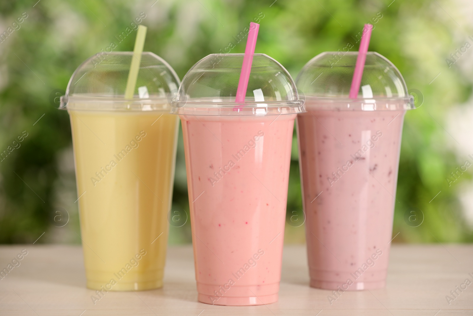 Photo of Plastic cups with different tasty smoothies on wooden table outdoors