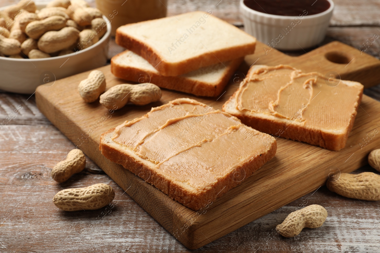 Photo of Tasty peanut butter sandwiches and peanuts on wooden table, closeup