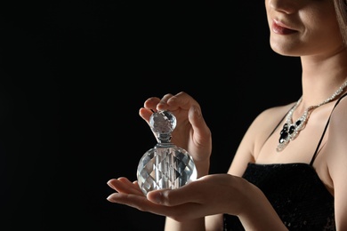 Young woman with bottle of perfume on black background, closeup. Space for text