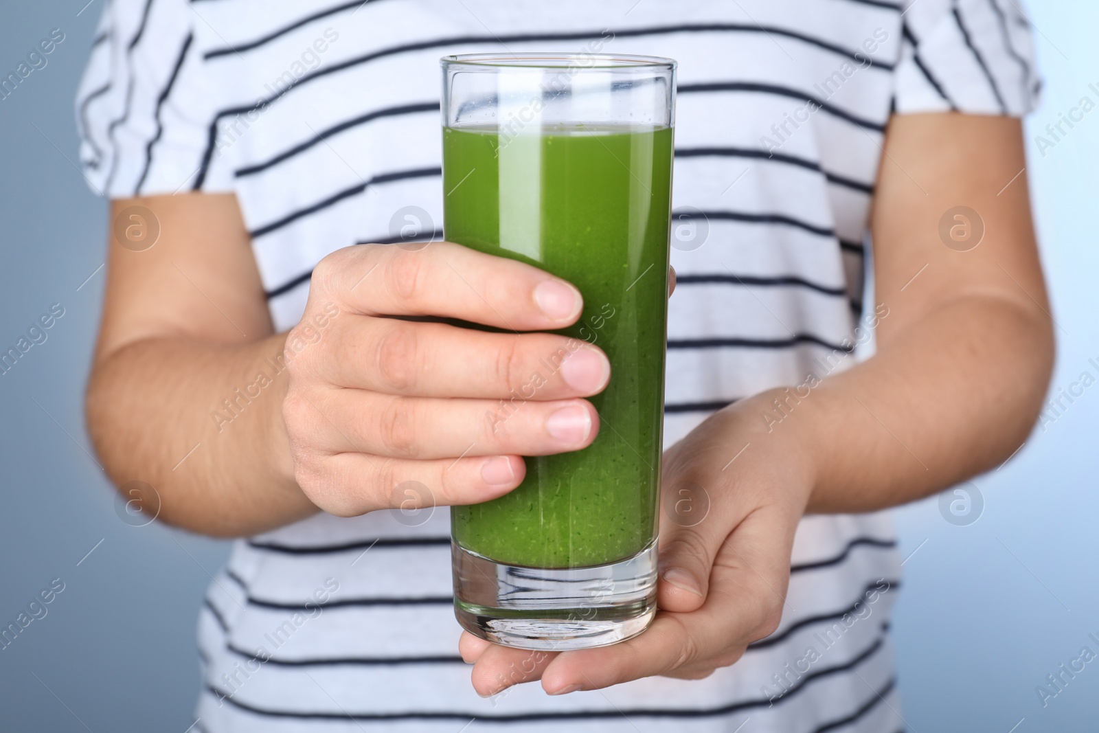 Photo of Woman holding glass with fresh celery juice on light blue background, closeup