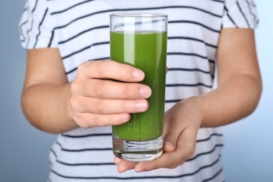 Photo of Woman holding glass with fresh celery juice on light blue background, closeup