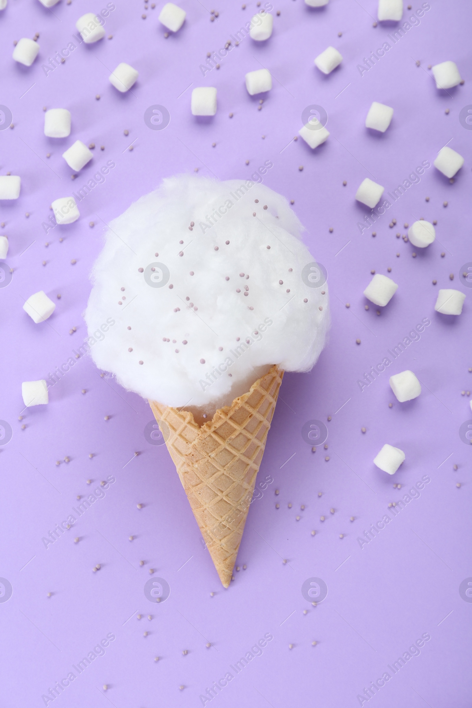 Photo of Sweet cotton candy in waffle cone and marshmallows on purple background, flat lay