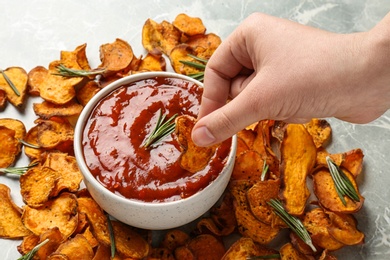 Photo of Woman dipping sweet potato chip in red sauce at table, closeup