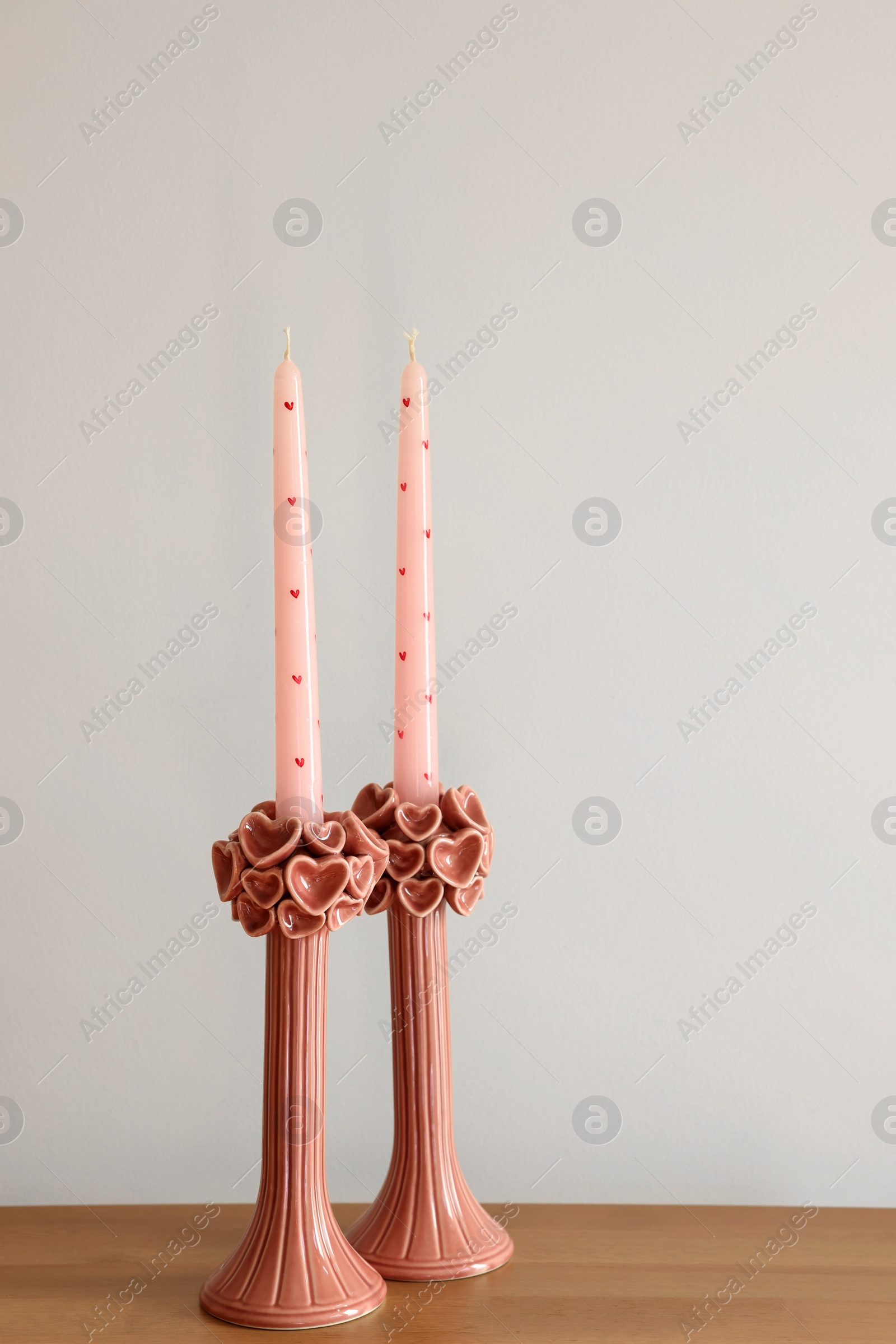 Photo of Beautiful pink wax candles on wooden table near white wall