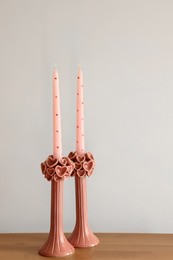 Photo of Beautiful pink wax candles on wooden table near white wall